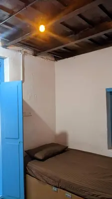 a small room with a bed and a refrigerator at Crossroads Hostel 1957 in Wayanad