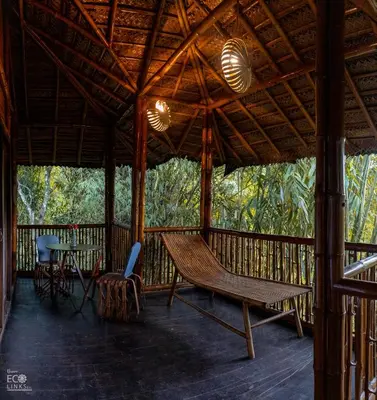 a porch with a hammock and a table and chairs at Uravu Bamboo Grove Resort in Wayanad