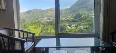 a glass table and a chair in front of a window at Velus Bungalow Ooty in Ooty