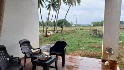 a porch with chairs and a table and a view of a field at SHI's Unique & Private 180 Degree Glass House in Pollachi in Pollāchi