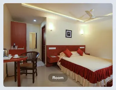 a bedroom with a bed and a table and a desk at Hotel Sasthapuri in Kozhikode