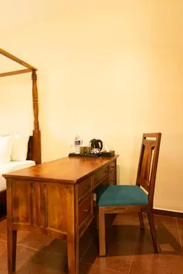 a wooden desk with a chair next to a bed at Ibex River Resort, Pollachi in Coimbatore
