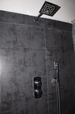 a shower in a bathroom with a black tile wall at Coorg Happy Estate Stay in Madikeri