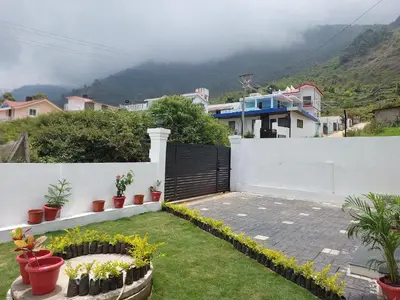 a backyard with a white fence and some plants at Kodai Diva Inn - Home Stay in Kodaikānāl
