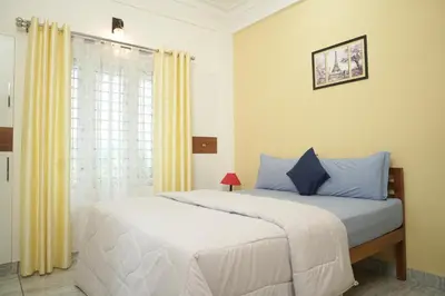 a bedroom with a bed with blue pillows and a window at AVANTI CASTELLO in Guruvāyūr