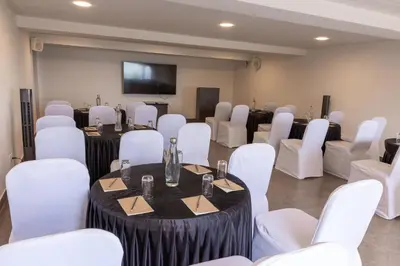 a room with white chairs and tables and a flat screen tv at Dvara Luxury Resort Kodaikanal in Kodaikānāl