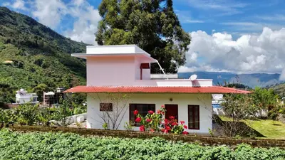 a small white house with red flowers on a hill at Mountain Mansion Kodai in Kodaikānāl