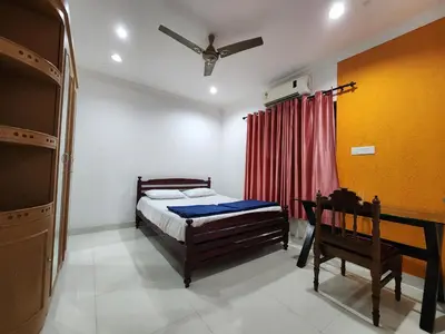 a bedroom with a bed and a table and a ceiling fan at Navarang Villa in Kalpetta