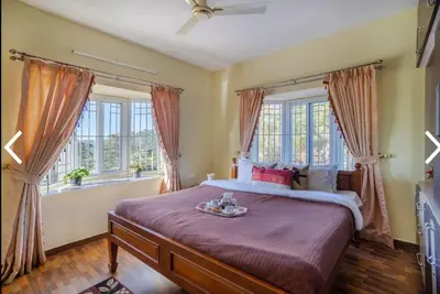 a bedroom with a large bed and two windows at MOUNTAIN OF MAGICS in Ooty