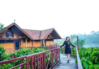 a woman walking down a wooden walkway in front of a building at Niyatma Wayanad Pool Resort by VOYE HOMES - Inside Coffee Plantation in Wayanad