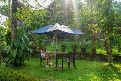 a woman sitting at a table under an umbrella at Niyatma Wayanad Pool Resort by VOYE HOMES - Inside Coffee Plantation in Wayanad