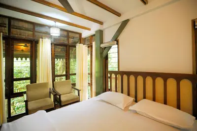 a bedroom with a bed and a chair and windows at Solitude Munnar - Tree house in Munnar