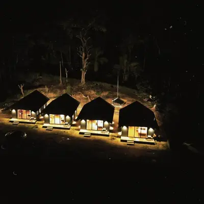 a group of lodges with lights at night at Bendheka - Cliff Front Cottages Coorg in Gonikoppal