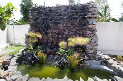 a stone wall with a pond in a yard at StayVista at Ivory Hill Madikeri including breakfast 3 Bhk Villa in Madikeri